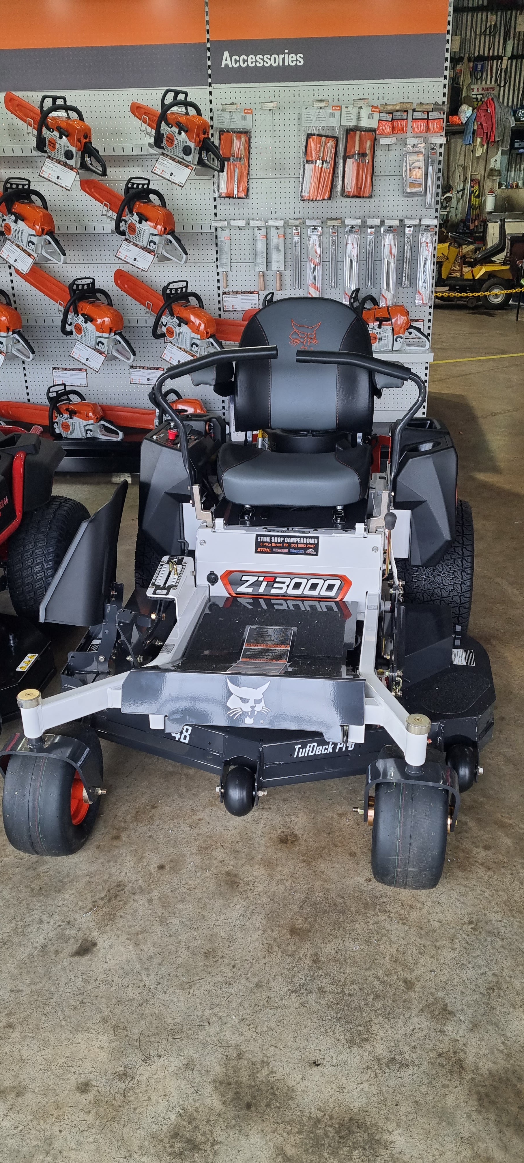 A Bobcat ZT3000 zero turn mower with a 48 inch TufDeck Pro deck on the workshop floor, in front of a wall of Stihl chainsaws